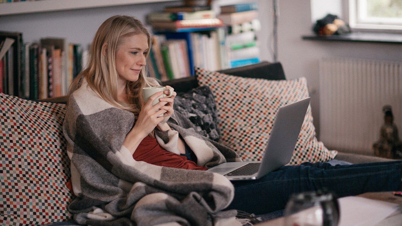 Jente med pledd og pc i sofa