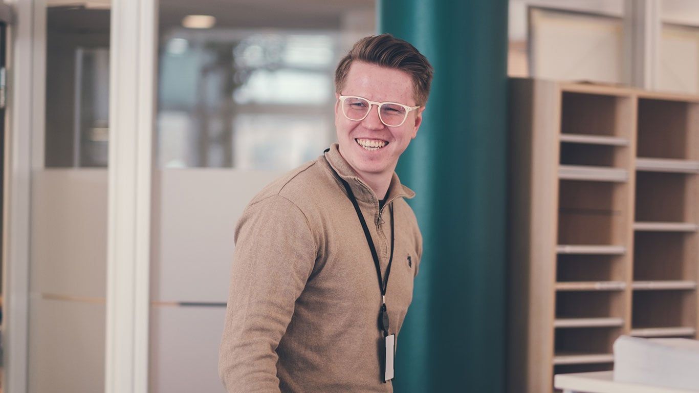 En smilende ung mann med briller i kontorlandskap