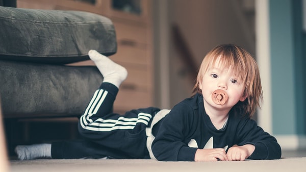 Liten gutt med smokk ligger på gulvet