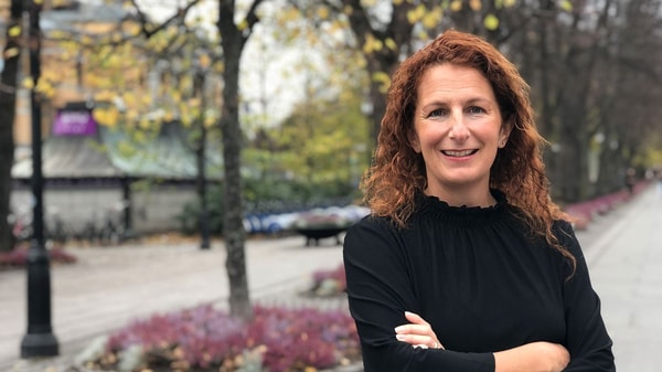 Kvinne i bygate, ser inn kameraet og smiler